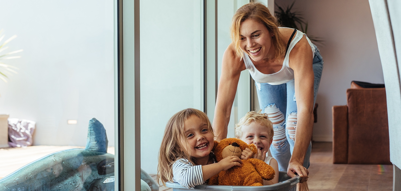Mother pushing her two small kids across floor in laundry basket