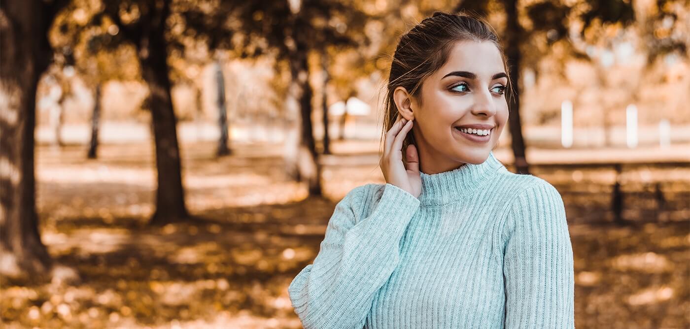Woman with ponytail and light green sweater smiling outdoors