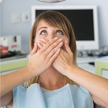 Woman in dental chair looking frightened and covering her mouth